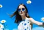 Placeholder: On a pop sky blue background, with embedded daisy flowers, a woman in a white dress, brunette, round sunglasses, 16K, real photography, advertising photography