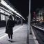 Placeholder: A beautiful slender Asian woman with short black hair and a black trench coat, waiting for a man at night at a train station in London