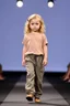 Placeholder: 2 years old beautiful baby blue eyes girl fashion model in loose pants and loose top with blonde curvy wavy hair ,cat walks in runway,catwalk and pose at end with cute
