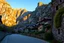 Placeholder: Medieval village from the perspective of a cobblestone road at sunset. The road and village continue to ascend into the mountains, with stone and wooden houses blending seamlessly into the rocky recesses of the mountain, reflecting the golden hues of the setting sun and the growing ivy. In the background, the majestic mountains feature large cultivated terraces and pronounced limestone gorges with hanging vegetation and meltwater streams.