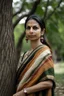 Placeholder: a beautiful 30 year old woman wearing a modern saree, standing near a tree, long face