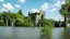 Placeholder: A ruined stone building in a lake, balconies, verandas, arches, bridges, spires, stairs, trees, dense foliage, spanish moss, ivy, blue sky, white clouds