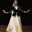 Placeholder: A graceful Azerbaijani female traditional dancer performing a famous Azerbaijani folk dance. She is wearing a beautiful traditional Azerbaijani dance costume: a long flowing silk dress with rich embroidery, wide skirt, and a colorful kelaghayi (traditional Azerbaijani silk headscarf) covering her head. The dancer moves elegantly with soft hand gestures, delicate finger movements, and smooth spinning steps typical of Azerbaijani women’s dances. The atmosphere is festive and cultural, with traditi