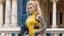 Placeholder: A happy modern Barbarella warrior with a machine gun covered by tattoos, 24-years-old her lean muscular frame wrapped in a yellow tactical bodysuit and a bullet proof vest over her bossom. Her blonde hair is pulled back in a tight ponytail, revealing blue eyes, she stands on the balcony of the marble palace of a modern dictator, behind we see the beach and palm trees [vintage style noisy scratches glitches, Shot the texture and then rewound the film and double exposed from a 1970 B series movie]