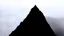 Placeholder: looking up at a single sharp narrow mountain, the peak obscured by clouds and fog.