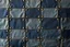 Placeholder: leather background covered with a grid of many rectangular weathered and faded canvas patches (navy blue) that are each stitched (brown) and nailed (brass) around the edges