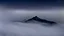 Placeholder: looking down at misty foreground and night sky background, no sun, single sharp narrow mountain peak coming through the mist in the center