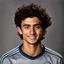 Placeholder: 85mm DSLR color photography of a very detailed headshot fitting all of head and hair in frame. 20-year-old Uruguayan soccer player, and with no facial hair and has no facial hair, has short and black hair with a small smile, grey background is in a Chelsea fc shirt