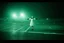 Placeholder: create a low-quality dashboard cam picture, high film grain, ghostly faceless girl in a white dress with arms extended levitating high off ground caught in headlights in an empty Wal-Mart parking lot on a foggy night, found footage, low contrast, super grainy greenish night vision hues, static haze.