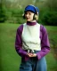 Placeholder: Everything she wear is in the image. of young woman, plum-blue-magenta-camouflage. She wears mantel and simple blouse.Felt cloth visor with tippet. SMALL FELT CAP is merged to Old AKG headphones with recognizable Golden rings! cloth materials are denim and felt cloth mixed. Fashion 1990's. Colors: Cream white, zinc plate, red ochre, ochre, orange - all mixed. Thick tights. Thick calves. She is in figure from top to toe.