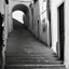 Placeholder: Calle de un pueblo de una isla italiana en verano, con escalinata, y arcos, tono decadente, fotografía real, fotografía realizada con cámara Leica y objetivo de 50 mm, siguiendo estilo de la serie 'Ripley', fotografía en blanco y negro, virada tonos años 50