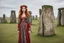 Placeholder: Full body shot of a tall slim red-headed young woman, dressed like a gipsy, standing in front of Stonehenge