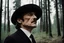Placeholder: A man in a shoulder-length black suit. the man's head in profile to the right. The head is raised, looking up. the mouth is slightly open. On his head is a black hat. White collar. Forest in the background. The style of Andrei Tarkovsky's films