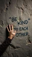 Placeholder: A hand writing On cave wall written “BE KIND “ “ TO EACH OTHER “ , an old man with bear and king hair wrote by the cave wall , a dim lighting great quality picture with primitive style
