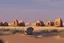 Placeholder: alien buildings, in the desert, surrounded by acacia trees, dunes, pathways, lake, roads, mountains, blue sky