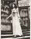 Placeholder: full-length, young woman dressed like a modern-day witch, floaty clothing, with dark hair, outside a shop