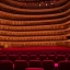 Placeholder: a single chair on stage under spotlight close up view facing empty audience at a dark and empty symphony hall