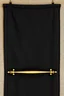 Placeholder: darker textured hanging fabric background with decorative brass corners at top, and a wide decorative brass bar clamped across the bottom