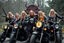 Placeholder: a very hard and tuff motorcycle young gang with long blond viking hair, not old, posing with their Harley Davidsson bikes, some of them holding guns and shotguns, a logo sign with Falköpings HD Club, "Fearless sinners" Skulls and bones, skeletons and fire DEMONS
