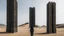 Placeholder: Person dressed in a burqa walks between rectangular towers of different heights in a desolate desert landscape.