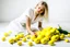 Placeholder: Sobre un fondo blanco de fotografía de estudio, un mujer rubia, vestida con camisa blanca sin abotonar y una amplia falda amarilla, juega con unos limones, por el suelo hay más limones