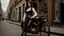 Placeholder: full-height portrait of a woman with straight shoulder-length black hair, with metal arms and legs, dressed in leather trousers, and a waistcoat, in a Victorian street next to a steampunk bike