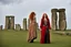 Placeholder: A tall slim red-headed woman, dressed like a gipsy, standing in front of Stonehenge