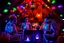 Placeholder: Glowing Halloween skeletons having a tea party in the haunted house attic. Colorful string lights and festive decorations create a spooky magical atmosphere