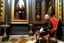 Placeholder: man with red beard sitting in a gothic armchair, golden armrests with trim, In the background a painting by Caravaggio covers the wall