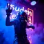 Placeholder: An "suden kebabia" performing at dance club, his name is "suden kebabia" and looks crazy, looks very aggressive look, Neon lights and smog, "suden kebabia" SIGN ON WALL