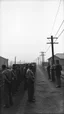 Placeholder: An old picture style black and white mono very bad quality looks very old camera picture with cracks of prisoners standing in line for food beyond bare wires in a Nazi concentration camps year 1900 in the background foggy clouds