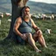 Placeholder: close up of a 40 year old Sardinian shepherd, sturdy, muscular and bulky, with short beard and big nose, relaxes sitting leaning against a tree in the middle of a meadow full of grazing sheep, dressed in a tank top and shorts, strong and muscular legs, bare feet, photorealistic bucolic scene,