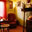 Placeholder: Flash photo of a room, 1980 horror movieshot, with chair, table, odd objects in background, ugly and scary mask, odd paintings hanging in the walls, rotten fruits, pair of glasses, horns, skin