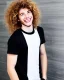 Placeholder: A skinny and high guy with wild curly blond hair, smiling with teeth and wearing black skinny jeans and a t-shirt