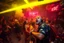 Placeholder: dans golv på en nedsliten sunkig techno club, många personer som dansar, yppiga kvinnor, mycket scen rök i lokalen, och gula röda strobes, en del personer ser in i kameran och skriker: "Benny!" och en Neon Skylt med texten "DJ ROY" på väggen, DJ Roy skriker rätt in i kameran, öppen mun, mycket flaskor och glas i baren