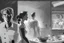 Placeholder: black and white storyboard, wide, on the Foreground there is a man and a girl in profile close to the camera, we see just part of their bodies passing by, and in the background, 3 chefs, scattered throughout the kitchen cooking, frying, cutting