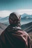 Placeholder: photo with a man distant from the camera with his face covered by a scarf wrapped around his head with space mountains in the background