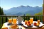 Placeholder: breakfast on a table on the terrace (orange juice, coffee in a cup, fruit, pastries), view of the mountains in the distance