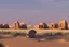 Placeholder: alien buildings, in the desert, surrounded by acacia trees, dunes, pathways, lake, roads, mountains, blue sky