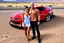 Placeholder: make a pic with short hair and little bald bodybuilder Knut Spildrejorde from Norway and his fitness wife Jeanette, they are standing front of his new red car Chevrolet Camaro, very busy highway in sunny desert Texas in the background