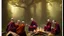 Placeholder: Black robed monks sitting around a fire in the forest