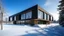 Placeholder: A modern building with a flat roof and large windows, set in a snowy landscape under a clear blue sky. The building features a combination of dark brick and wood paneling, with a section that extends out over the ground level. The windows are tall and narrow, providing a view of the interior. The ground is covered in a thick layer of snow, and there are a few bare trees scattered around the building. In the distance, there are snow-covered hills. The lighting is bright and even, creating a sense