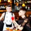 Placeholder: Russian guy boyish boylike short man's haircut boyish features in black girlish lacy cocktail dress as mother in restaurant