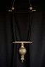 Placeholder: darker textured hanging fabric background, with decorative brass corners at top, and a heavy brass decorative element clamped across the bottom