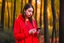 Placeholder: young woman in red clothing standing in a forest holding a smartphone