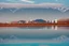 Placeholder: Sunny day, distant modern city, lake, lake reflections, people, mountains