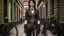 Placeholder: full-height portrait of a woman with straight shoulder-length black hair, with metal arms and legs, dressed in leather trousers, and a waistcoat, in a Victorian street next to a steampunk bike