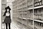 Placeholder: full-height shot of a young witch in a tight black short skirt, inside a large magic shop, shelving, bottles, windows