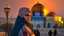 Placeholder: A Palestinian woman wearing an embroidered dress with the Dome of the Rock in front of her during sunset in winter.