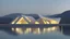 Placeholder: A modern architectural structure with irregularly shaped holes illuminated from within at night, a person standing in the doorway, and a body of water in the foreground with mountains in the background